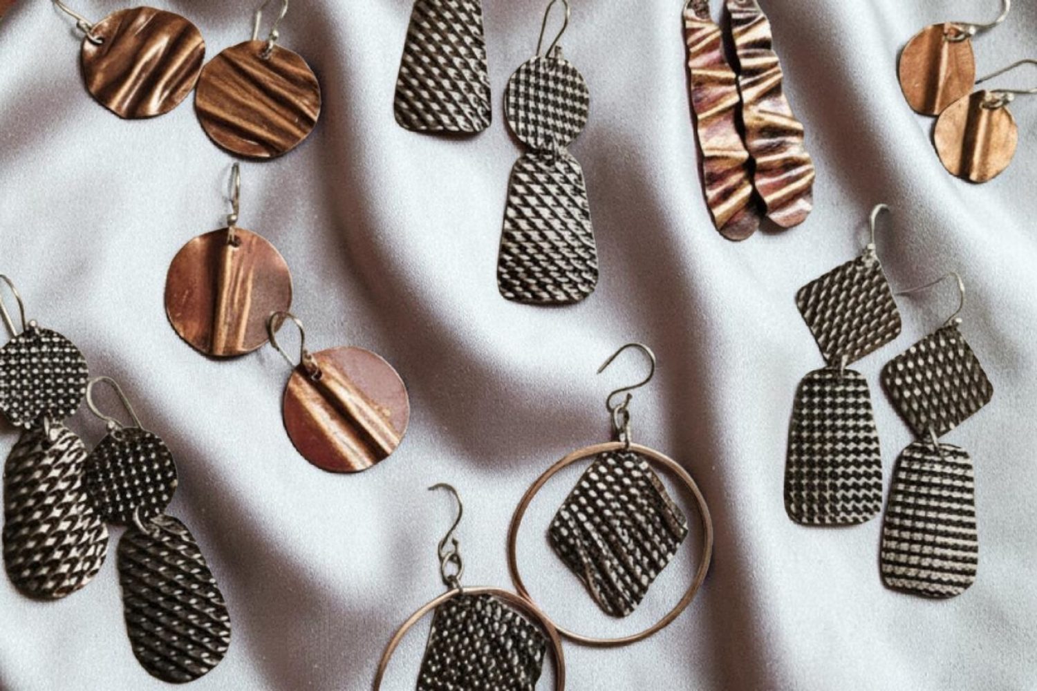 a collection of copper dangle earrings in many different shapes loaded with texture, ripples, and snake skin patterns