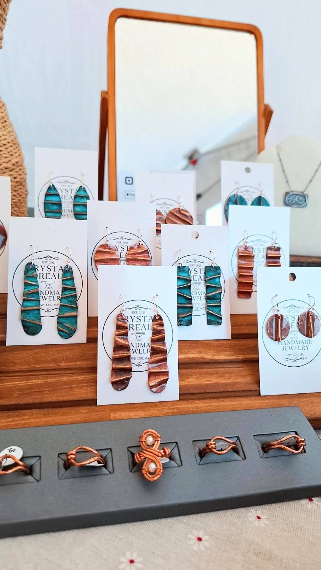 fire painted copper earrings, & green oxidized copper earrings, and copper rings. on display with a mirror in the background