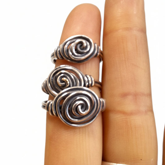 Three silver spiral ring on a finger against a textured green background