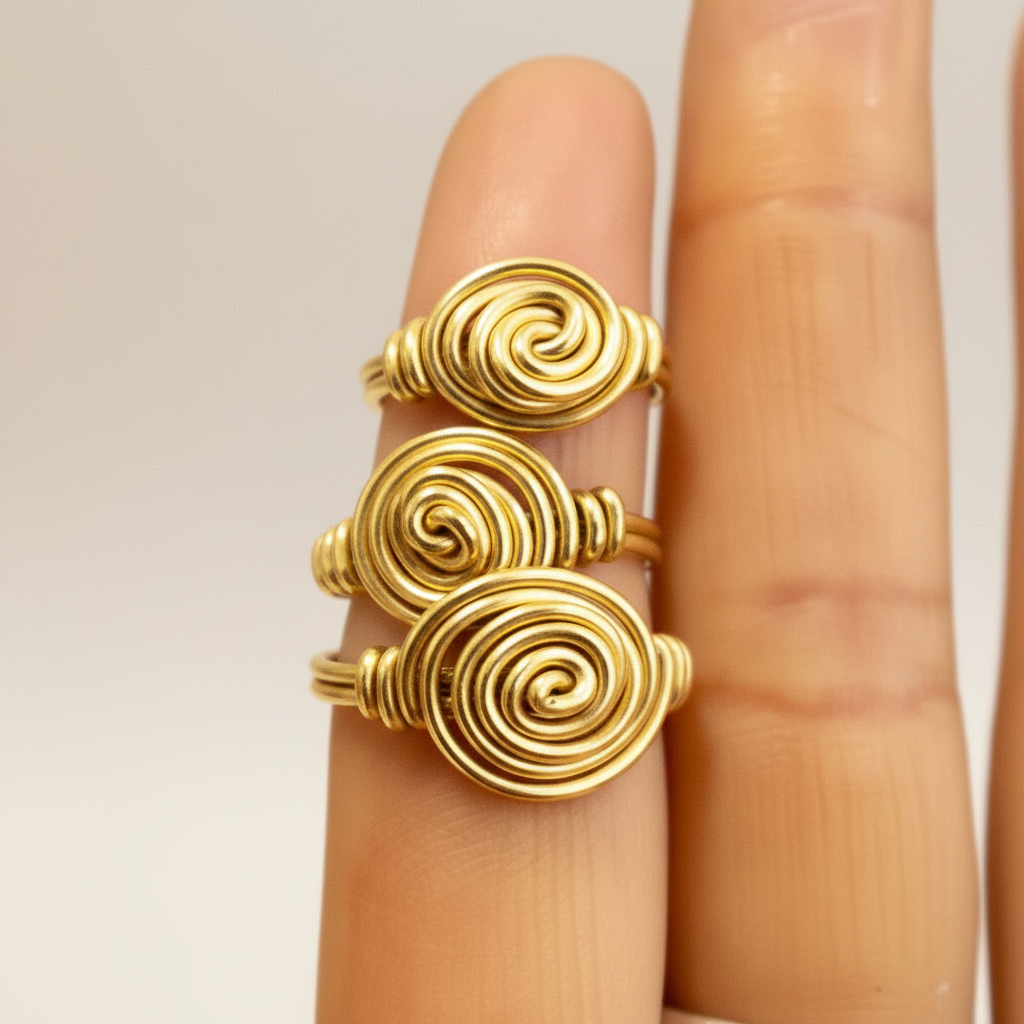 Three gold spiral rings on a finger against a neutral background