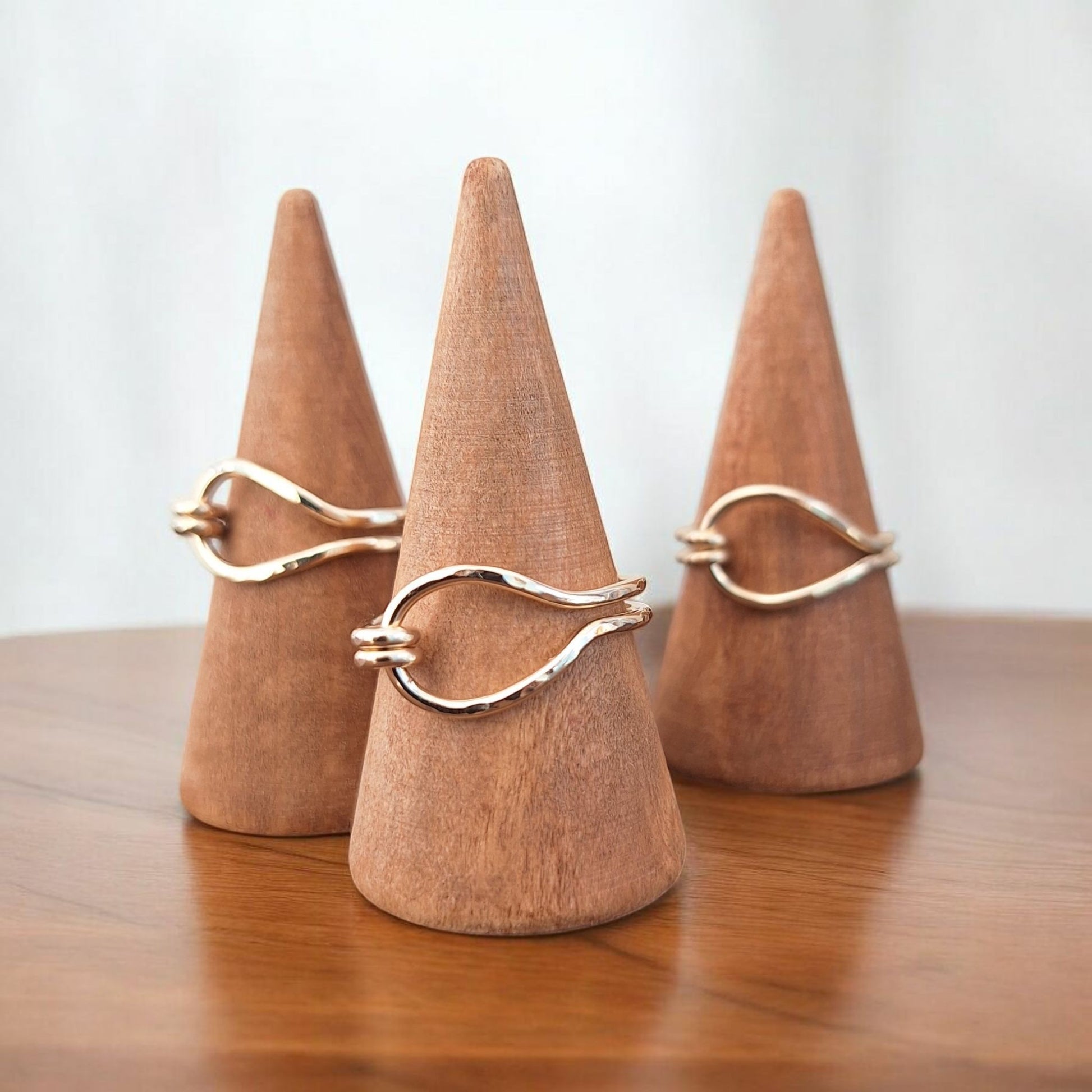 Three handmade gold knot rings on wooden cones against a white background
