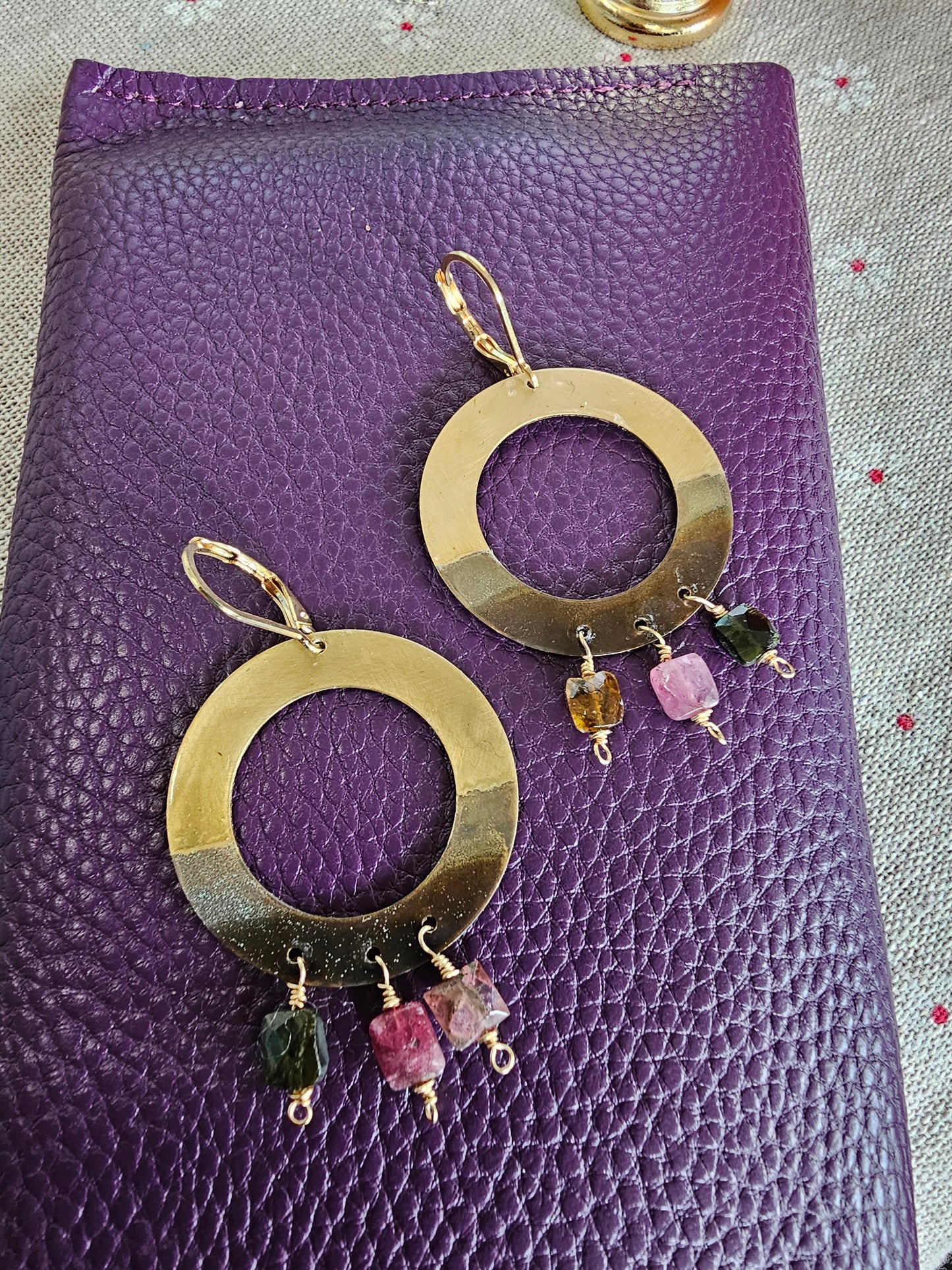 Gold hoop earrings with gemstones on a purple textured surface