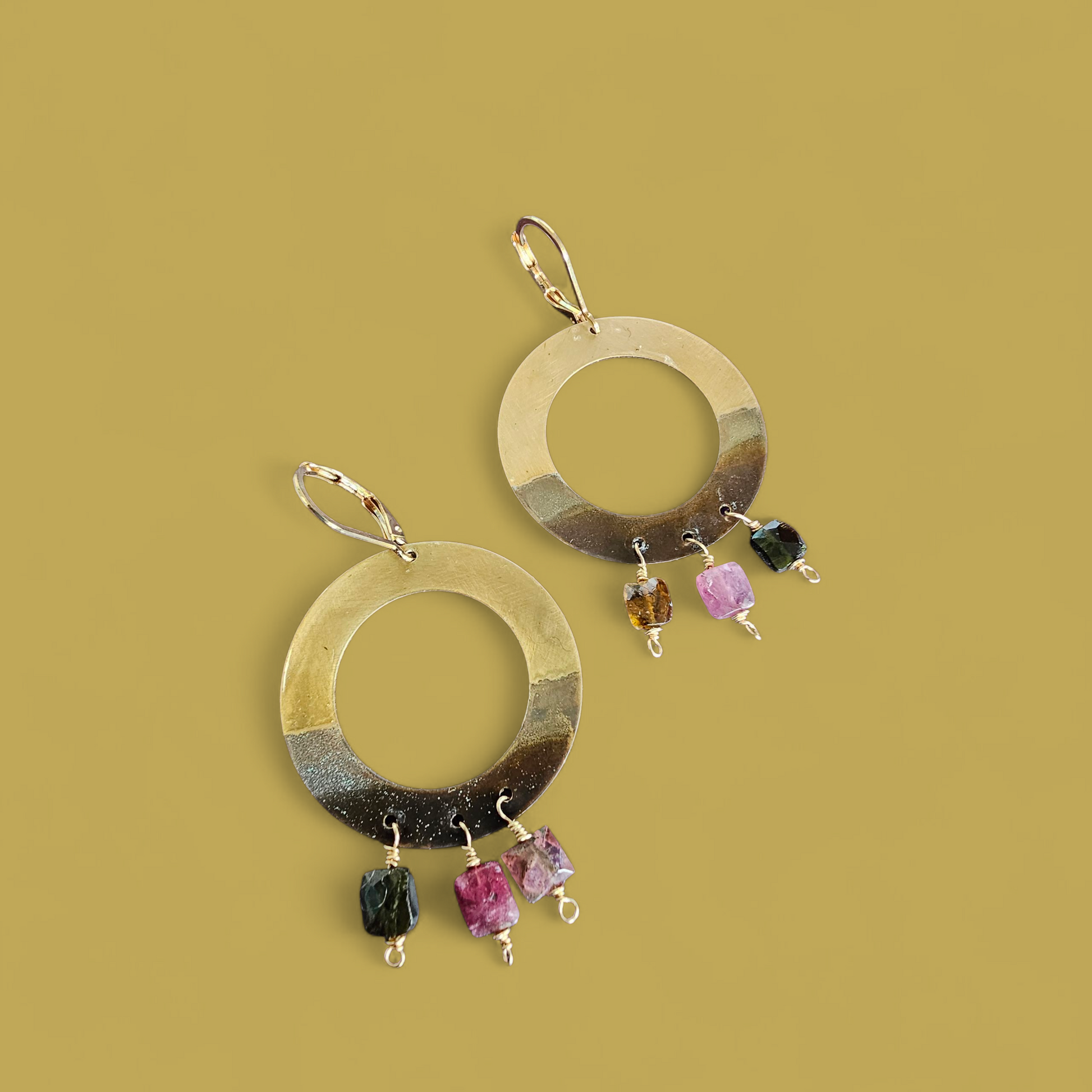 Gold hoop earrings with colorful beads on a mustard yellow background