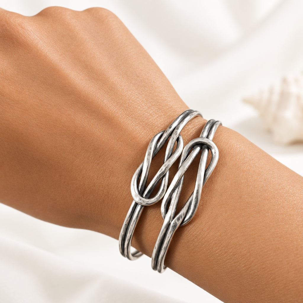 A close-up of a person's wrist wearing two interlocking silver cuff bracelets with a knotted, twisted design.