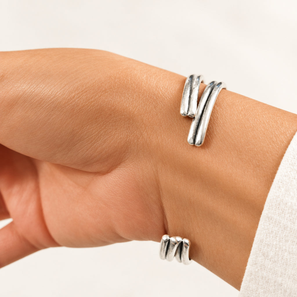 A close-up of a person's wrist wearing a silver wrap-style cuff bracelet with two parallel polished bands that curve around the wrist.