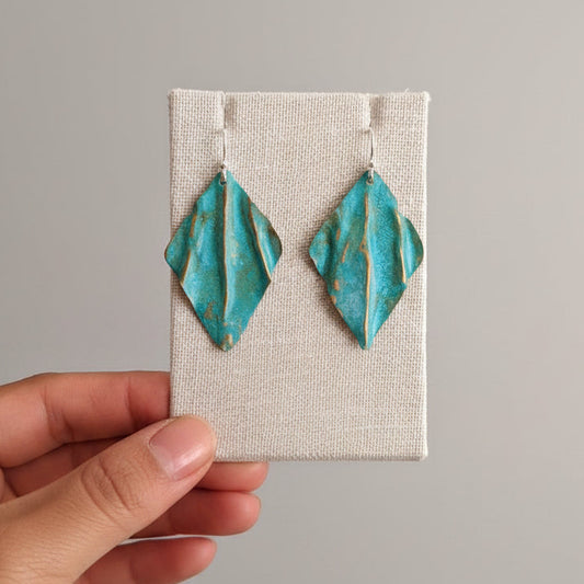 Turquoise earrings on a white card held by a hand against a blue curtain background