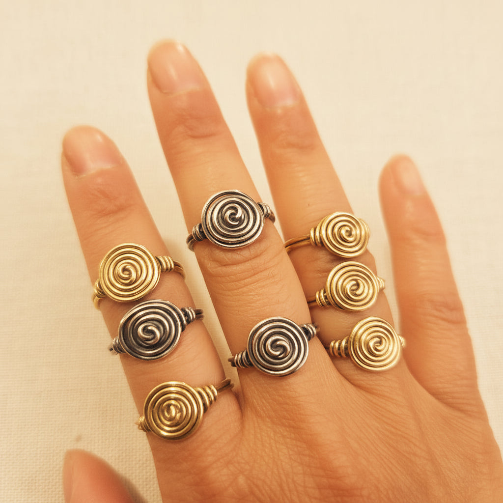 Hand wearing multiple spiral-patterned rings on a plain background